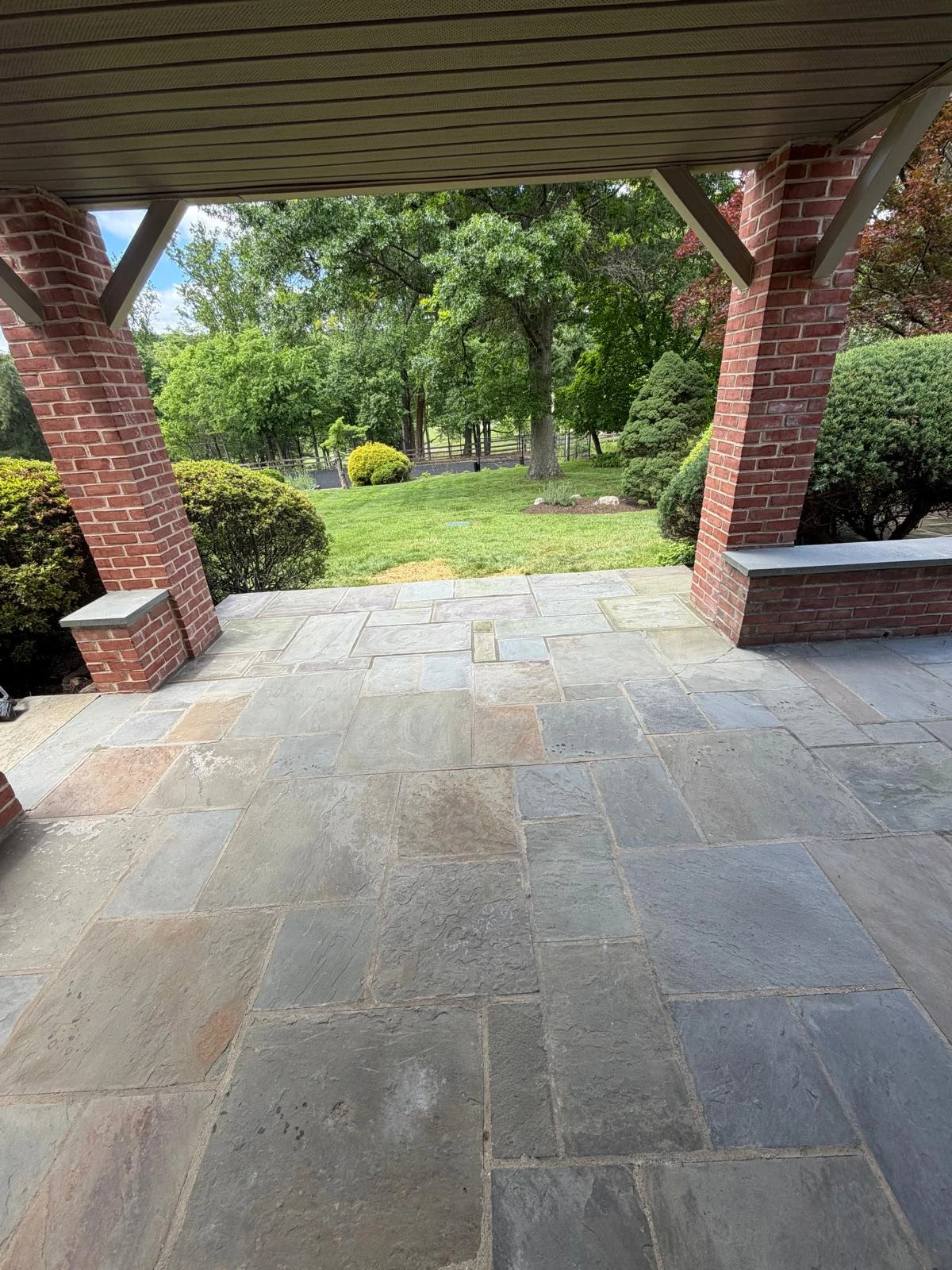 Stone patio beneath a covered porch with brick columns
